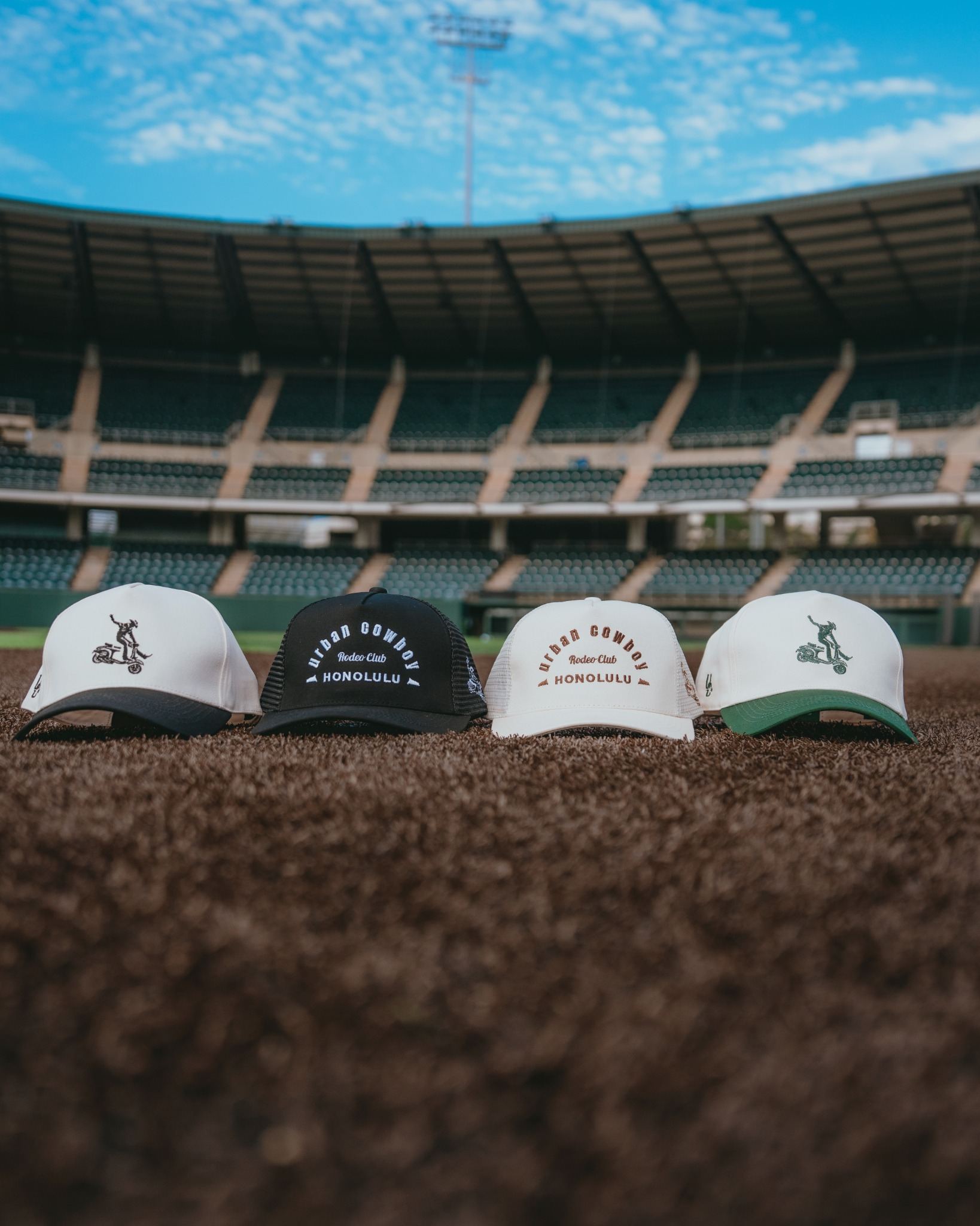 Four baseball caps on a grassy field with stadium seats in the background