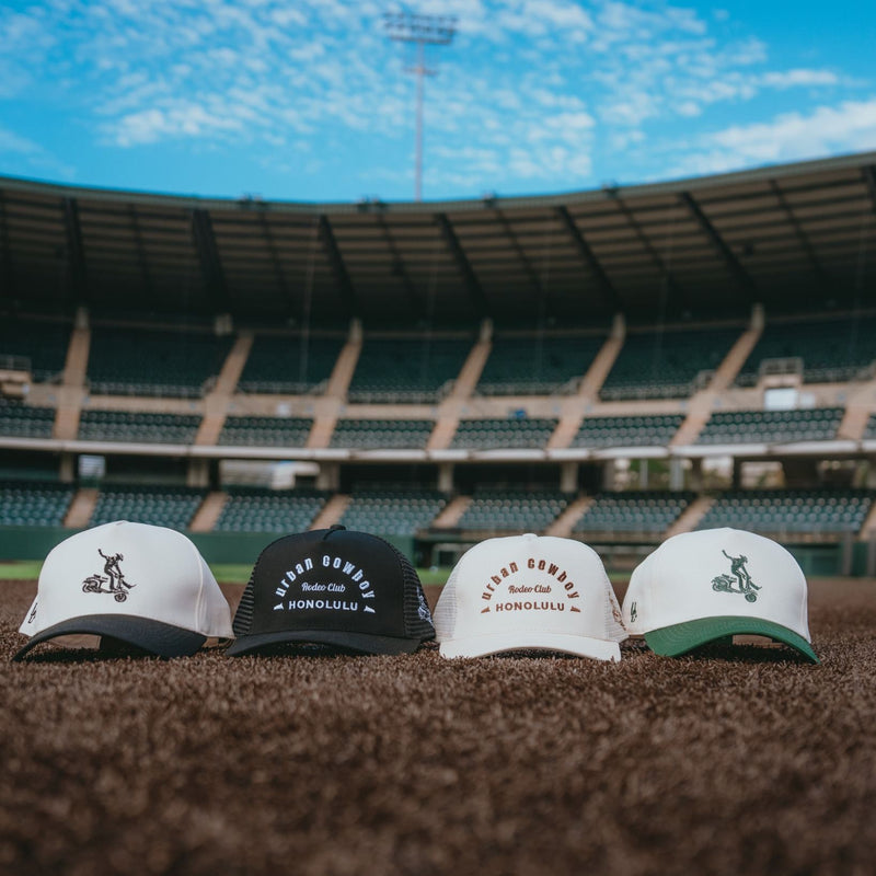 Four baseball caps on a grassy field with stadium seats in the background